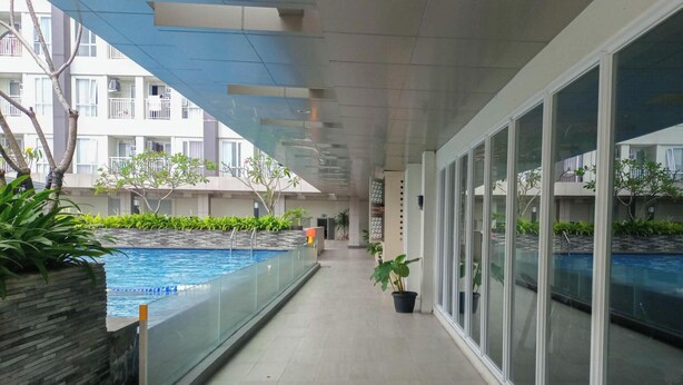 A corridor with a glass-enclosed swimming pool, potted plants, and a view of residential buildings.
