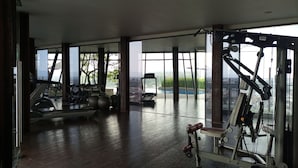 Ein Fitnessstudio mit Trainingsgeräten, großen Fenstern und Blick auf eine Stadtlandschaft.