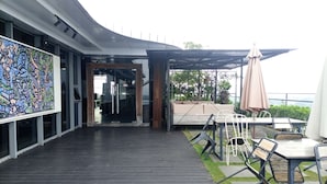 Ein Außenbereich mit einer Holzterrasse, Sitzgelegenheiten mit Tischen und Stühlen sowie ein großes, farbenfrohes Wandgemälde an der Gebäudefassade.
