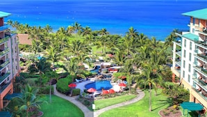 A resort with a pool area surrounded by palm trees, a view of the ocean, and multiple buildings with balconies. - KLVR welcomes you to Luana Garden Villa 1C upper level with partial ocean view  (Lahaina)