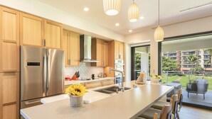 A modern kitchen with stainless steel appliances, a large island, and a view of a balcony with outdoor furniture. - KLVR welcomes you to Luana Garden Villa 1C upper level with partial ocean view  (Lahaina)