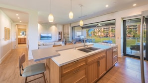 A modern kitchen with a large island, wooden cabinets, and pendant lighting.