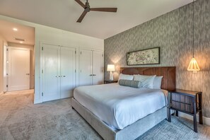 A bedroom with a large bed, a ceiling fan, a nightstand with a lamp, and a wardrobe.
