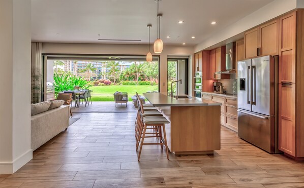 A modern kitchen with a large island, wooden cabinets, and a view of a lush garden.