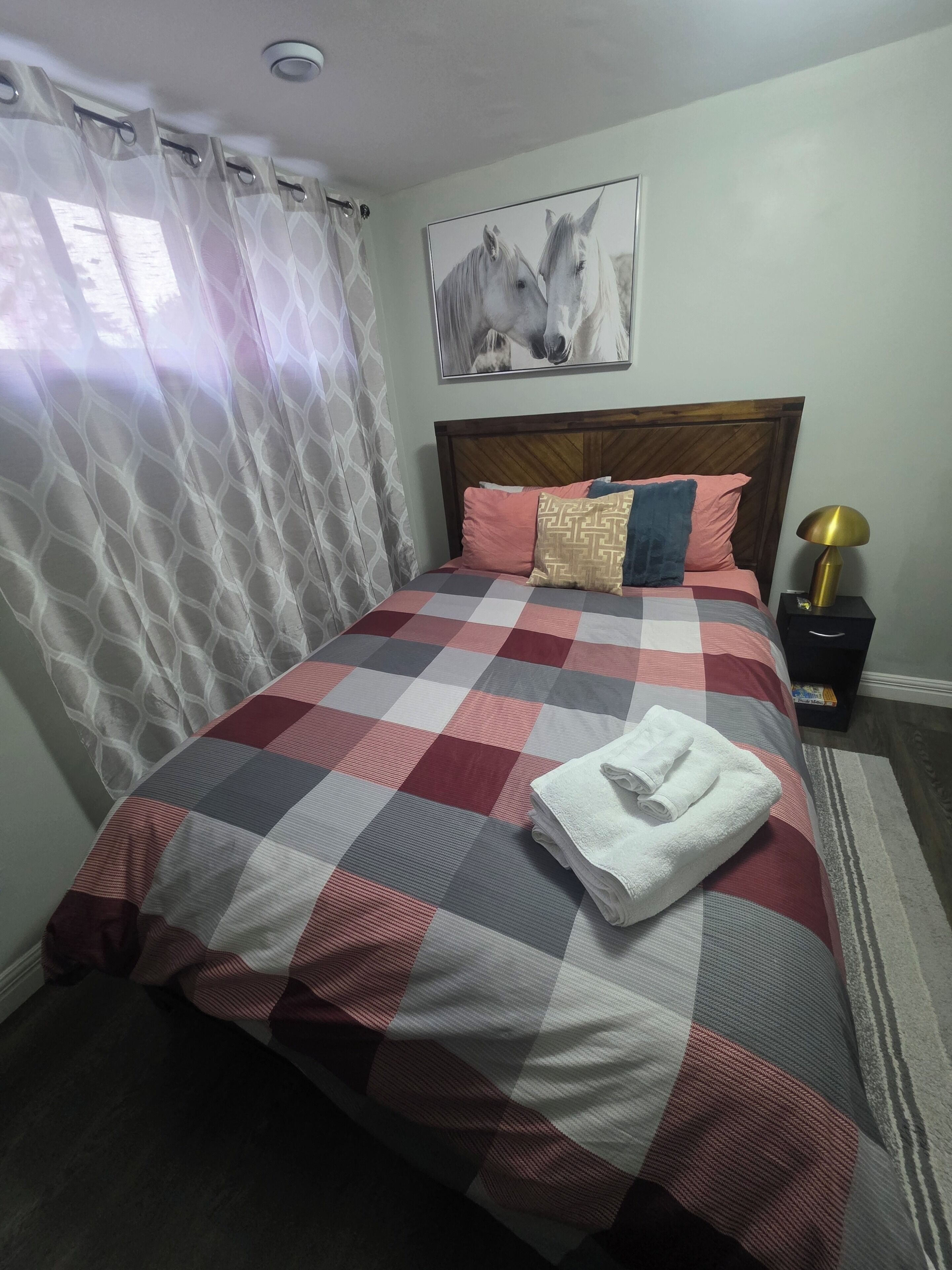 A neatly made bed with a checkered bedspread, a headboard, and a wall-mounted horse painting.