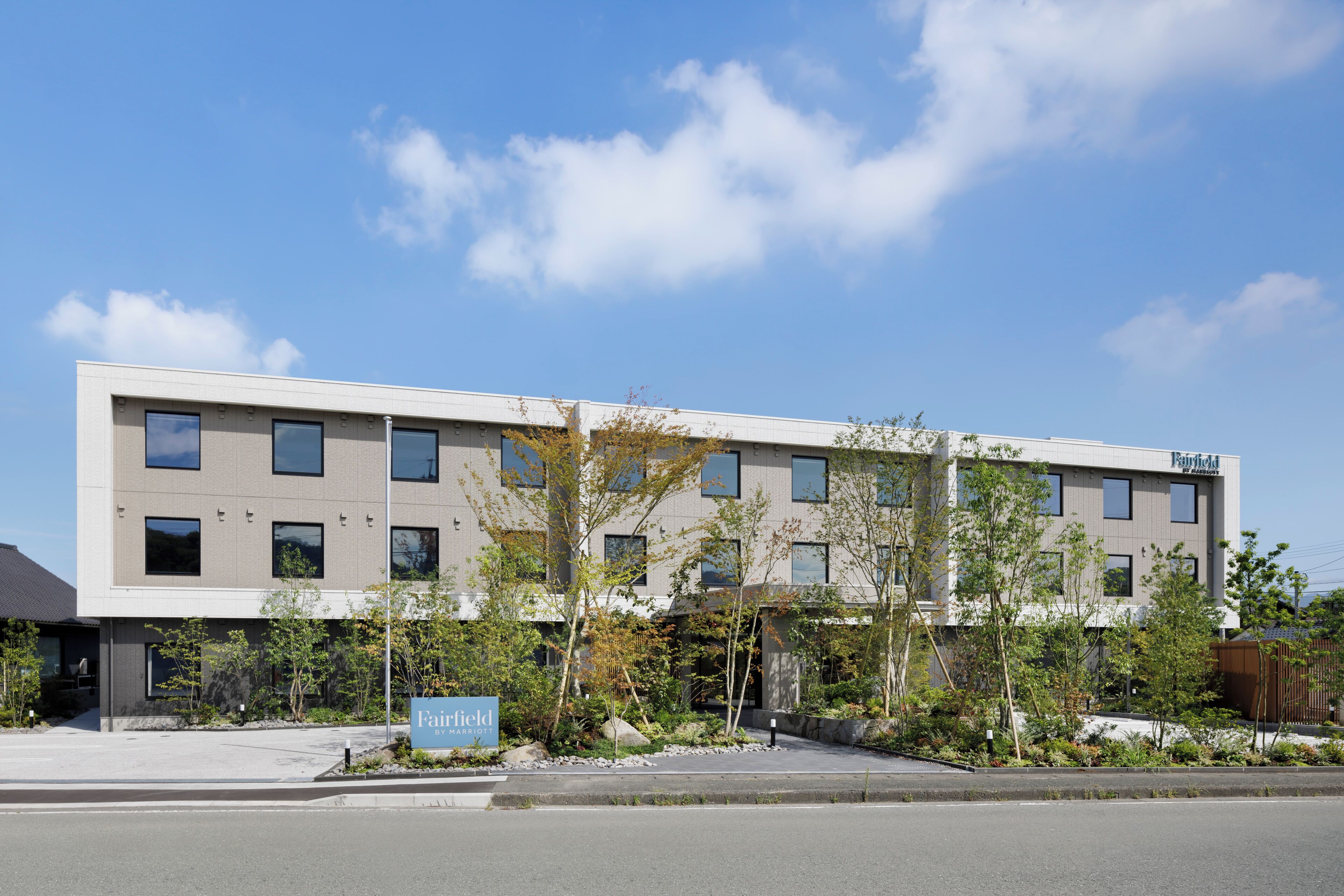 A modern hotel building with a flat roof, multiple windows, and a landscaped area with young trees.