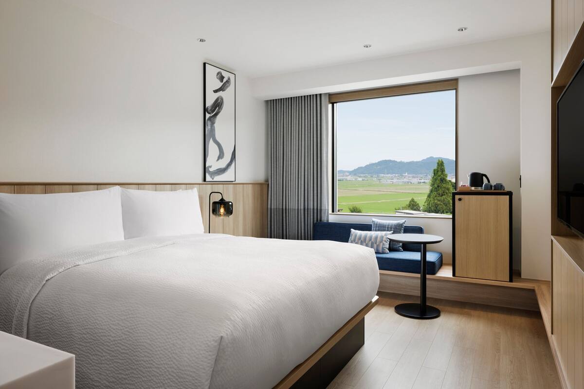 Une chambre d’hôtel moderne avec un grand lit, un coin salon près de la fenêtre et une télévision.