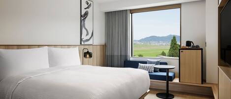 Ein modernes Hotelzimmer mit einem großen Bett, einer Sitzecke am Fenster und einem Fernseher.