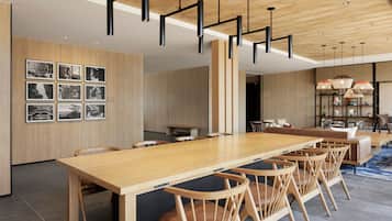 A modern dining area with a wooden table and chairs, a high ceiling with exposed beams, and a wall adorned with framed photographs.