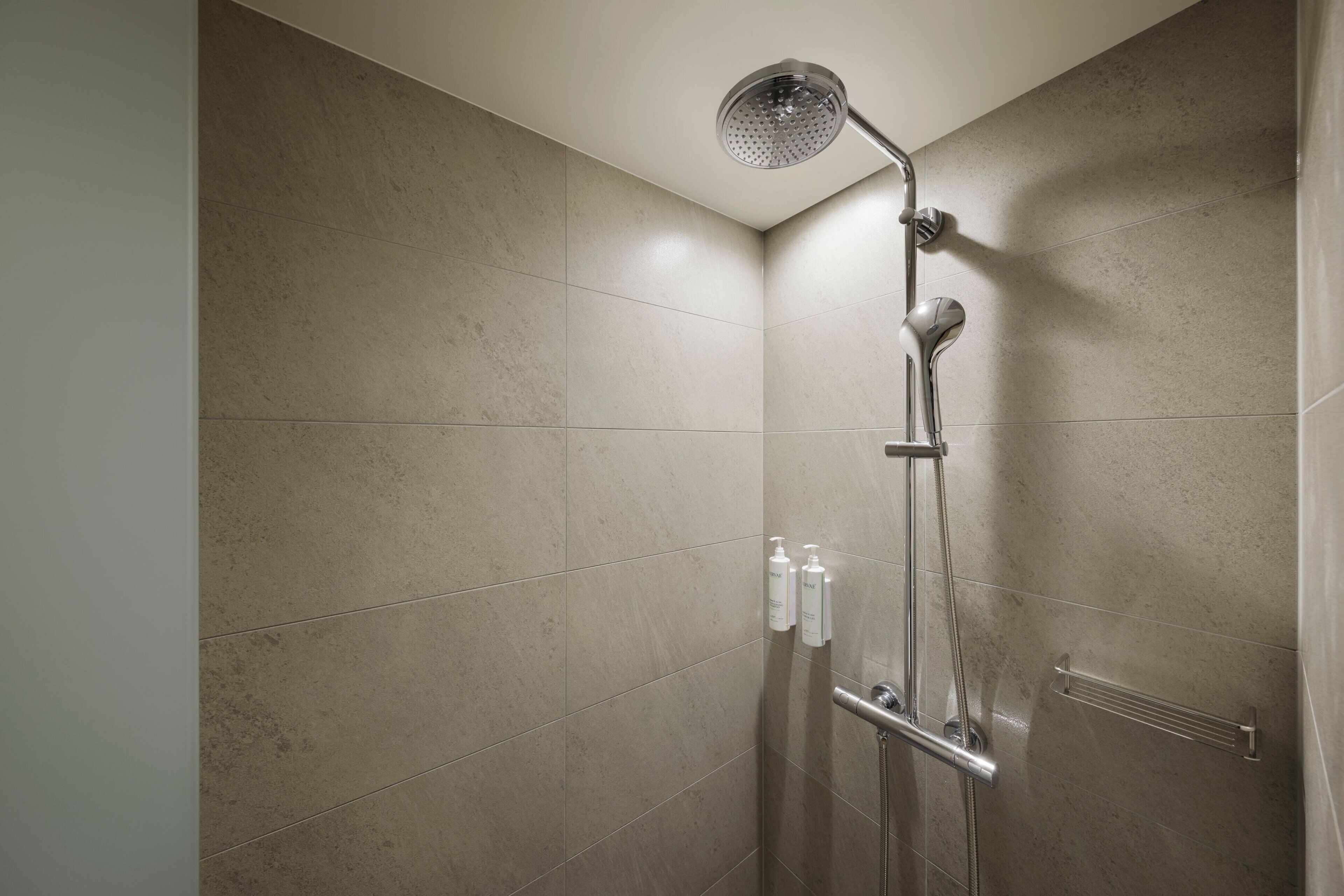 A shower with a handheld showerhead, a handheld showerhead, and a handheld showerhead.