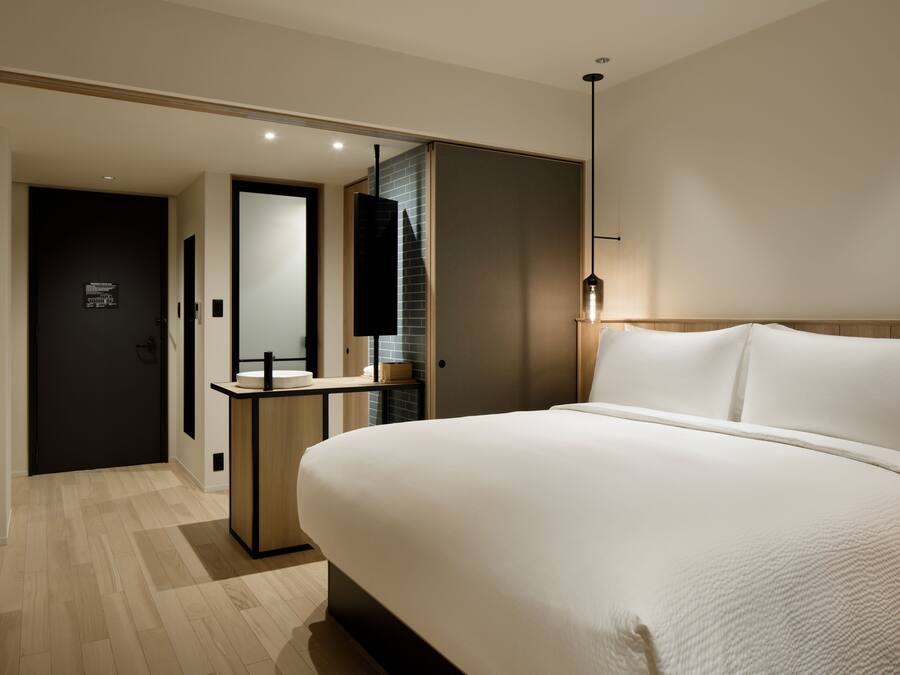A modern hotel room with a large bed, a bedside table, a mirror, and a small desk area.