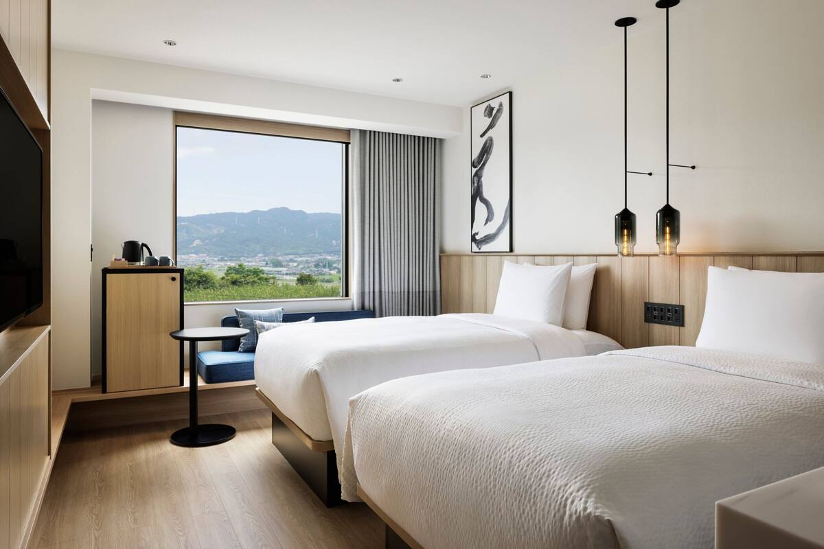 Une chambre d’hôtel avec deux lits, une grande fenêtre donnant sur un beau paysage, une petite table et un téléviseur.