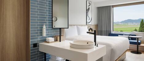 A modern hotel room with a large bed, a white sink, and a view of the countryside.