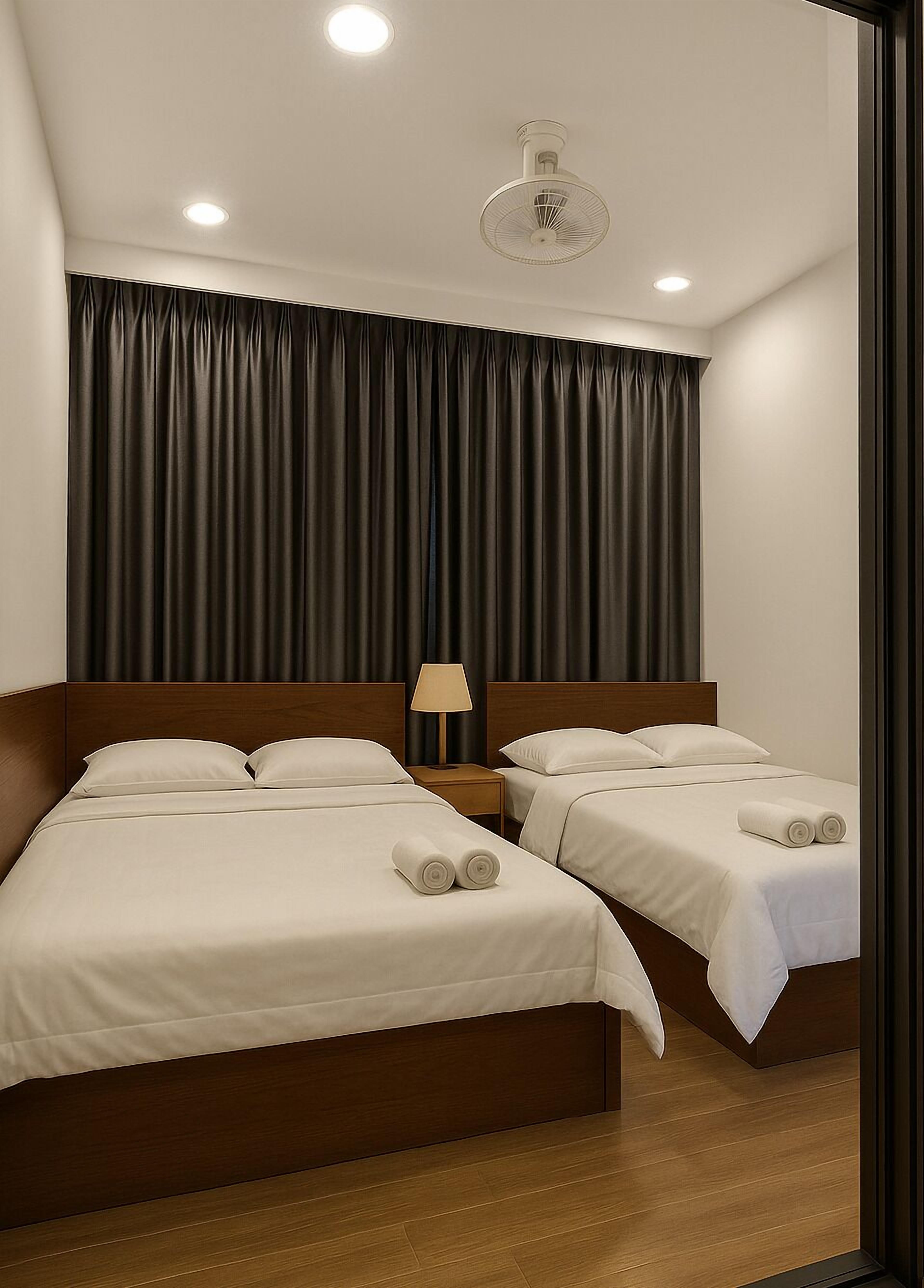A hotel room with two beds, a ceiling fan, and a window with dark curtains.
