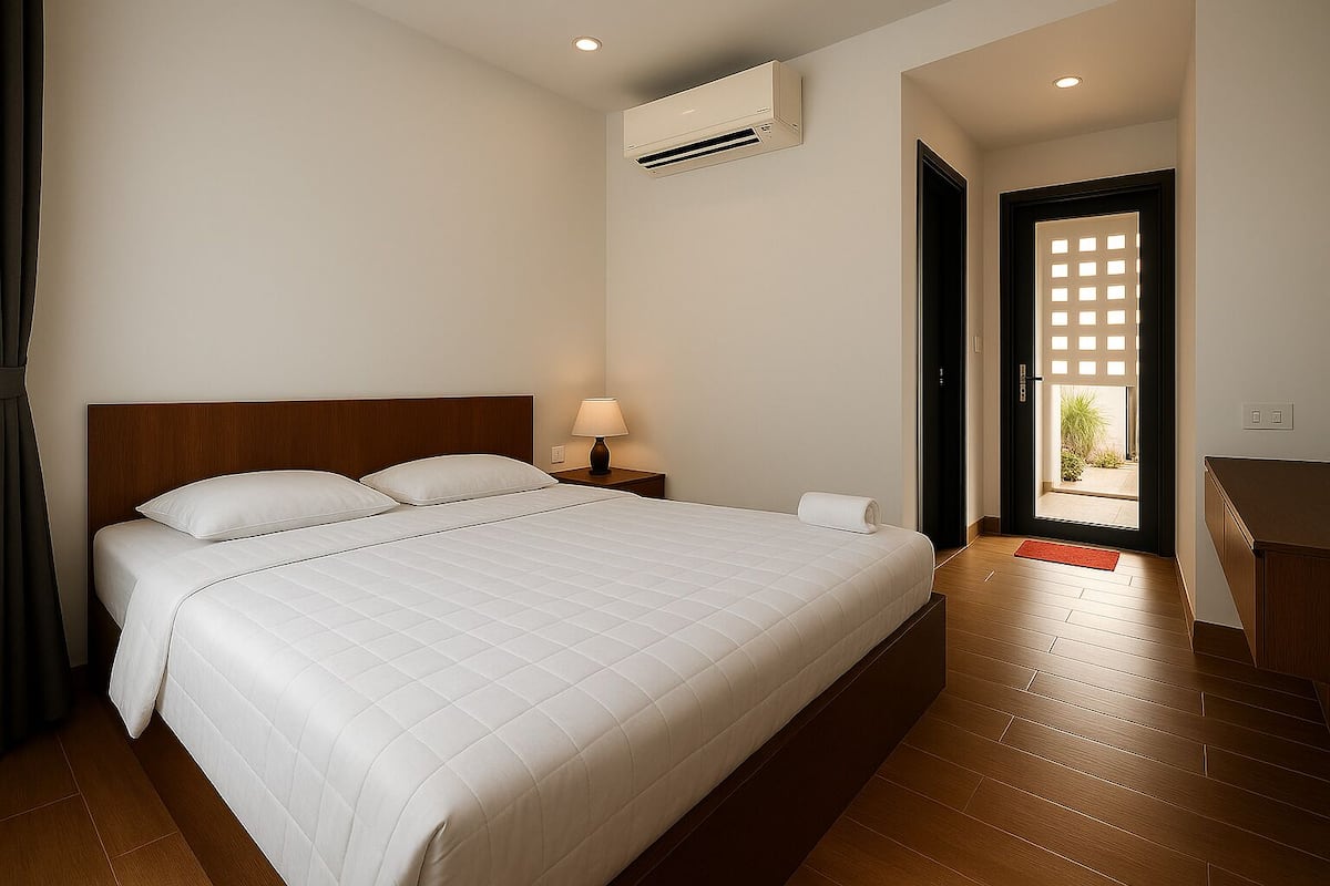 Une chambre d’hôtel avec un lit, une lampe de chevet, un appareil de climatisation et une vue sur l’extérieur, visible à travers une porte.