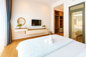 Quarto de hotel com uma cama, televisão, guarda-roupa de madeira e porta de correr de vidro.