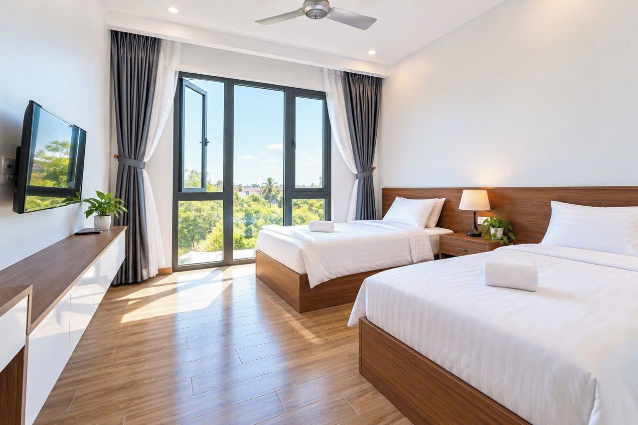 Habitación de hotel con una cama grande, una cama más pequeña, un escritorio con televisor y vistas a zonas verdes a través de las ventanas.