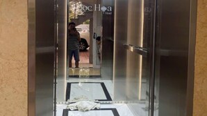 Een moderne lift met glazen deur, leidend naar een gang met een betegelde vloer en een zichtbaar logo voor 'Hotel Hoca'.