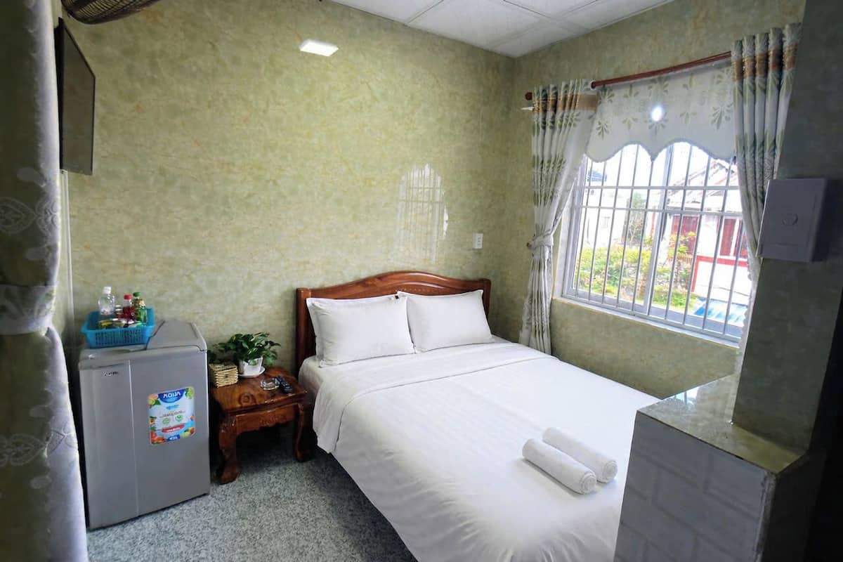 Une chambre d’hôtel comprenant un lit, un petit réfrigérateur, une table de chevet, une fenêtre avec des rideaux et une vue sur l’extérieur.