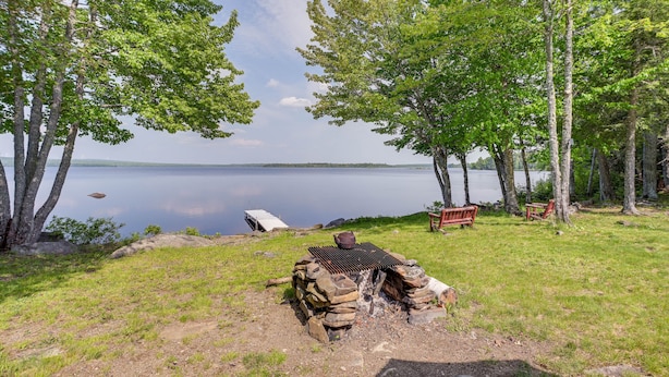En campingplats vid sjön med en eldstad, bänkar och ett tält.
