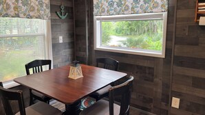 Un comedor con una mesa y sillas de madera, un farol decorativo y una ventana con vistas a la vegetación.
