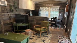 Una sala de estar acogedora con televisor, un sofá verde, una mesa de centro de madera y una alfombra estampada.