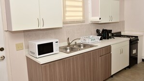Een moderne keuken met witte kastjes, een roestvrijstalen spoelbak, een magnetron, een fornuis en een raam met zonwering.