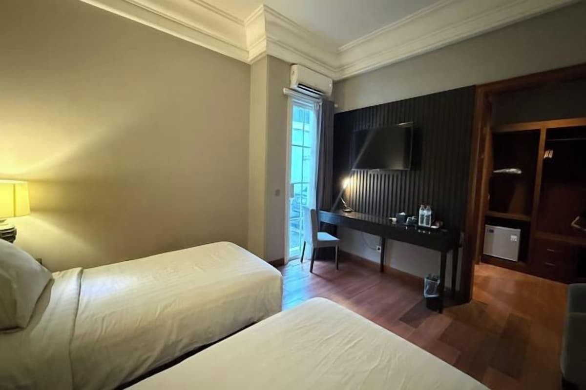 Una habitación de hotel con dos camas, un escritorio, una silla, un televisor y un armario.