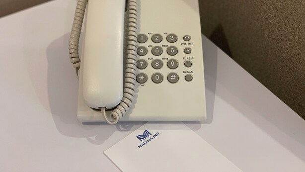 A Panasonic telephone on a white surface with a business card labeled "MADINA INN" beside it. - Madina Inn Hotel (Yogyakarta)
