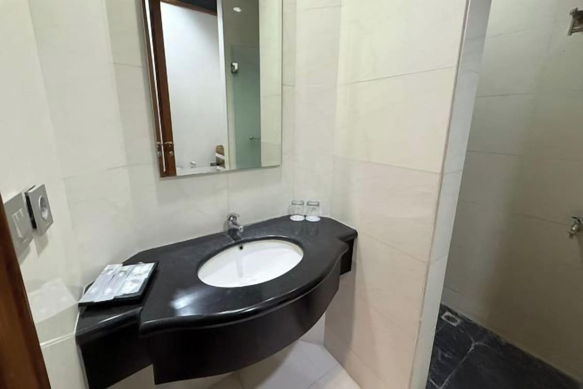 Un baño con un lavamanos negro, un espejo y una zona de ducha.