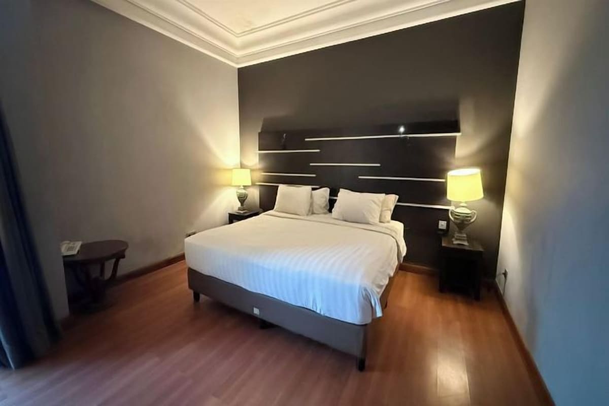 A modern hotel room with a large bed, two bedside tables with lamps, and a dark headboard.