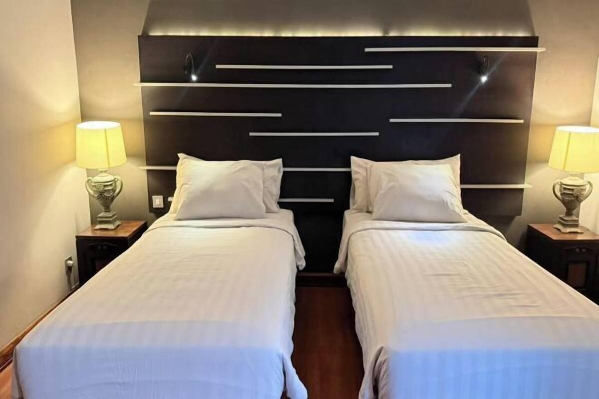Een hotelkamer met twee bedden, een modern hoofdeinde, nachtlampjes en een houten vloer.