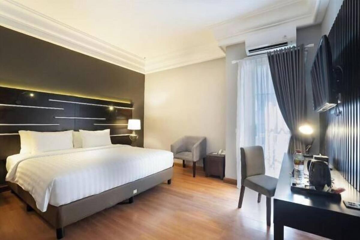 Een hotelkamer met een groot bed, een bureau, een stoel, een lamp en een airco.