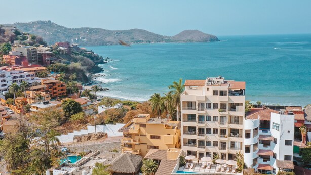 Un hôtel situé sur la côte, avec plusieurs étages, des balcons et un espace piscine.