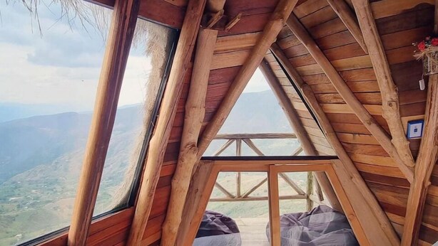 A wooden room with a sloped ceiling, a window overlooking a mountainous landscape, and a bed with a white duvet. - La Juanita Hostel Mesa de los Santos  (Los Santos)