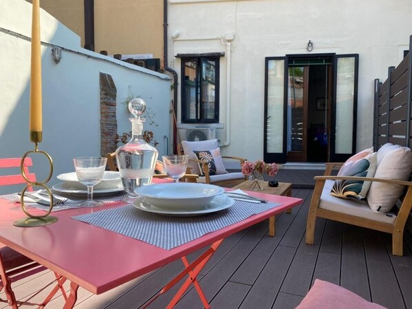 A red table set with plates, glasses, and a bottle, surrounded by wooden chairs and a bench with cushions.