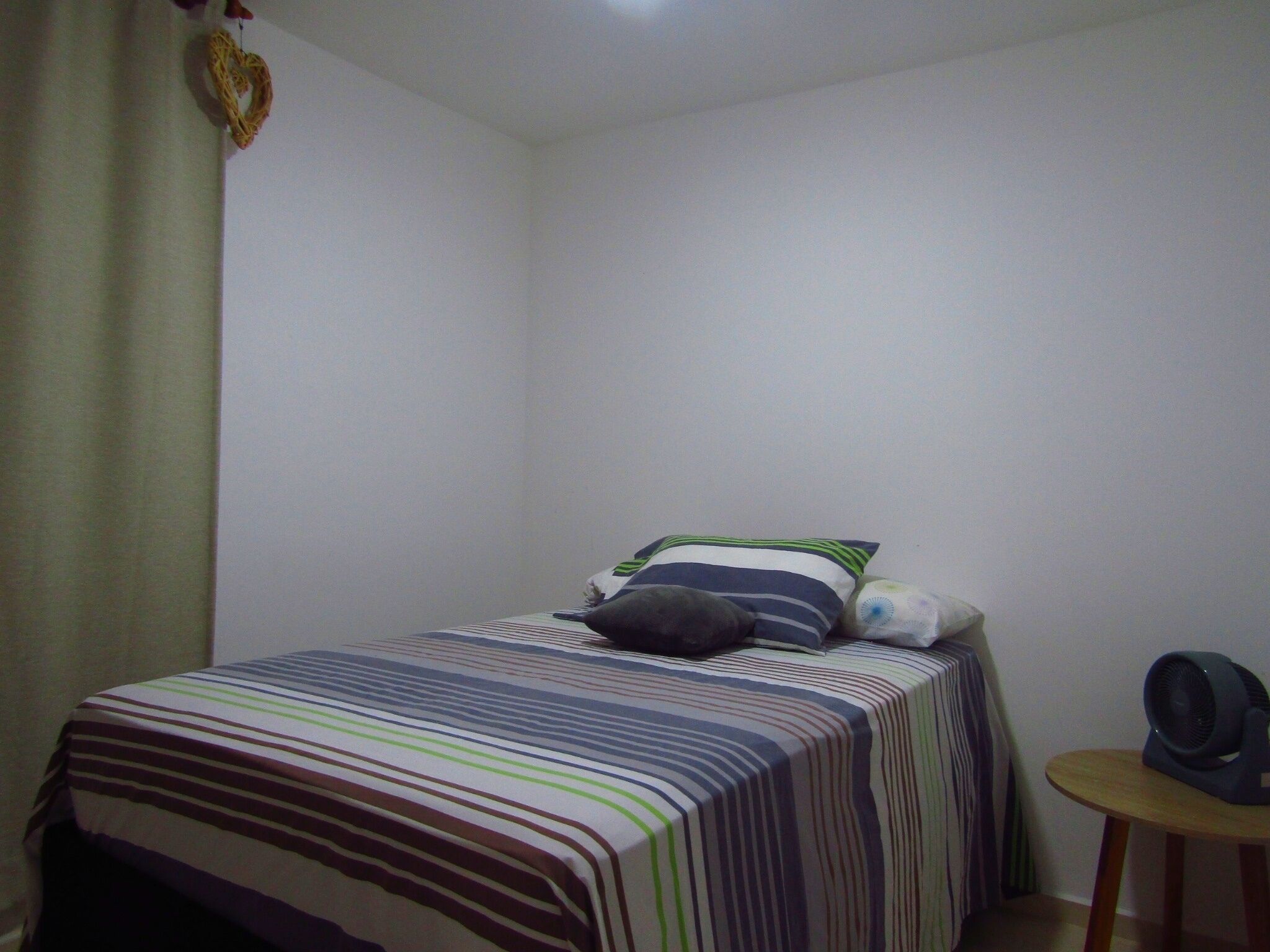 A small, sparsely furnished room with a single bed, a small table, and a fan.