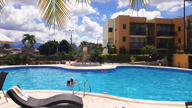 A swimming pool with lounge chairs and a palm tree in the foreground. - Modern apartment located in a resort style condo, pools, jacuzzi, soccer field,. (La Tebaida)