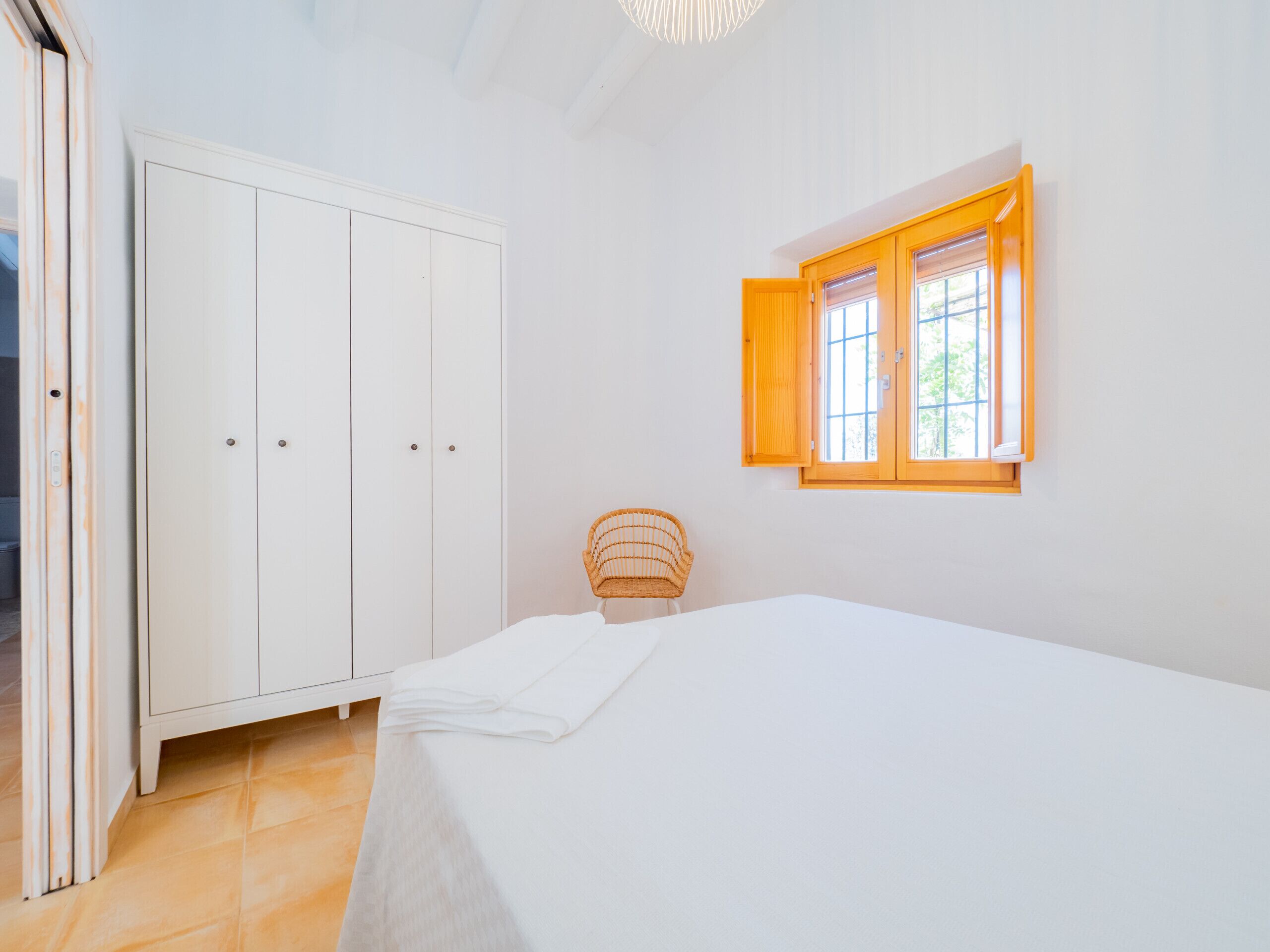 A bedroom with a bed, a wardrobe, a window, and a chair.