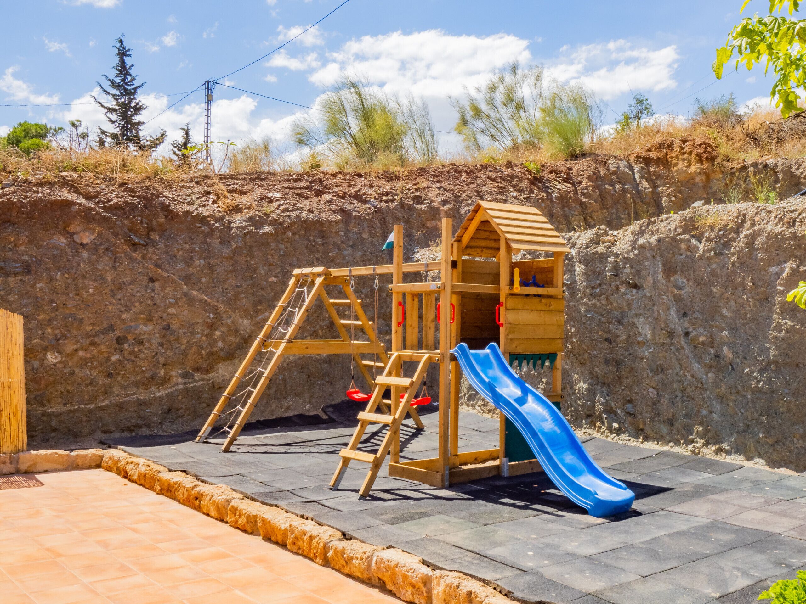 A wooden playhouse with a slide, set against a rocky hillside.