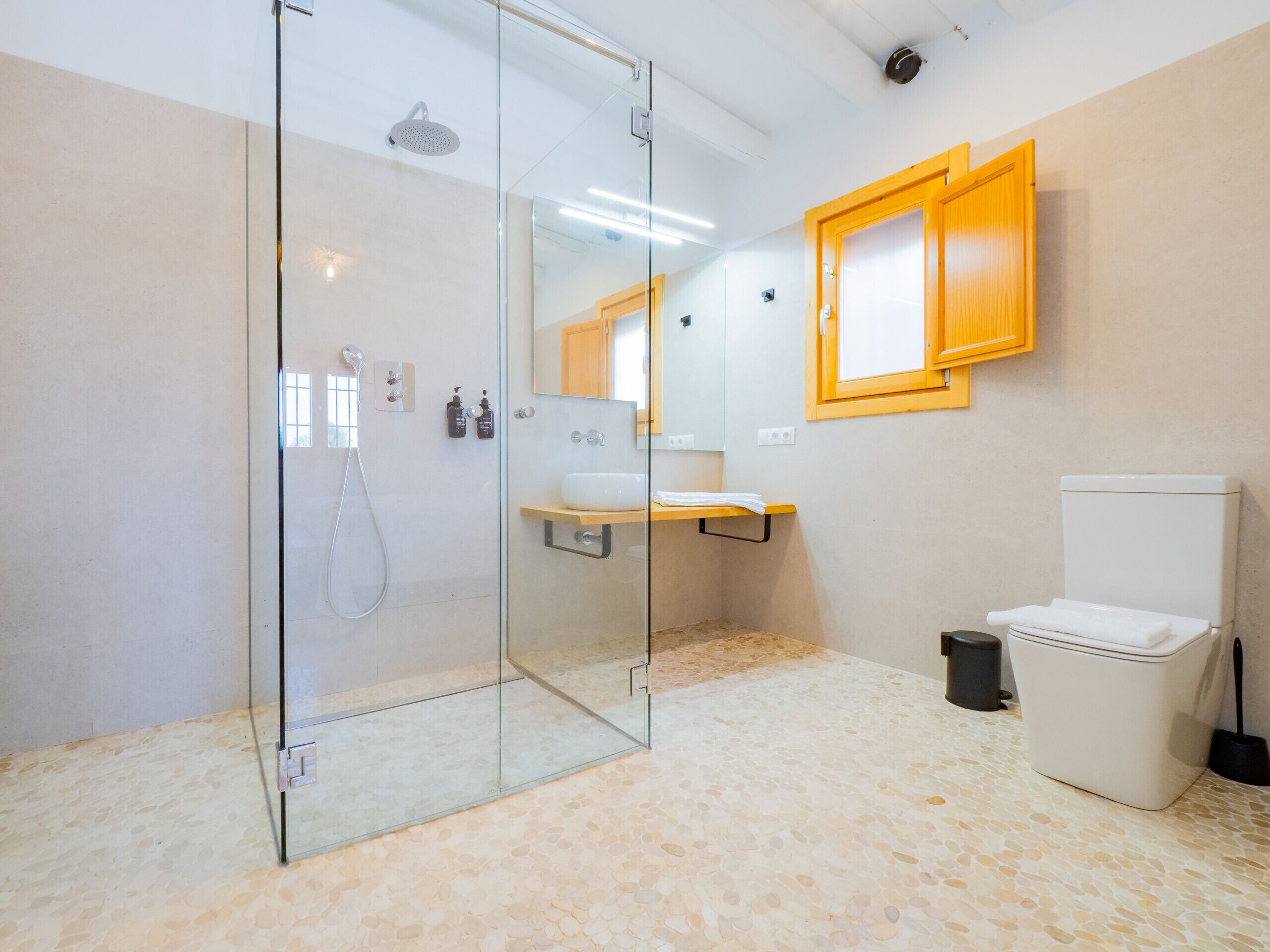 A modern bathroom with a glass-enclosed shower, a wooden medicine cabinet, a white sink, and a toilet.