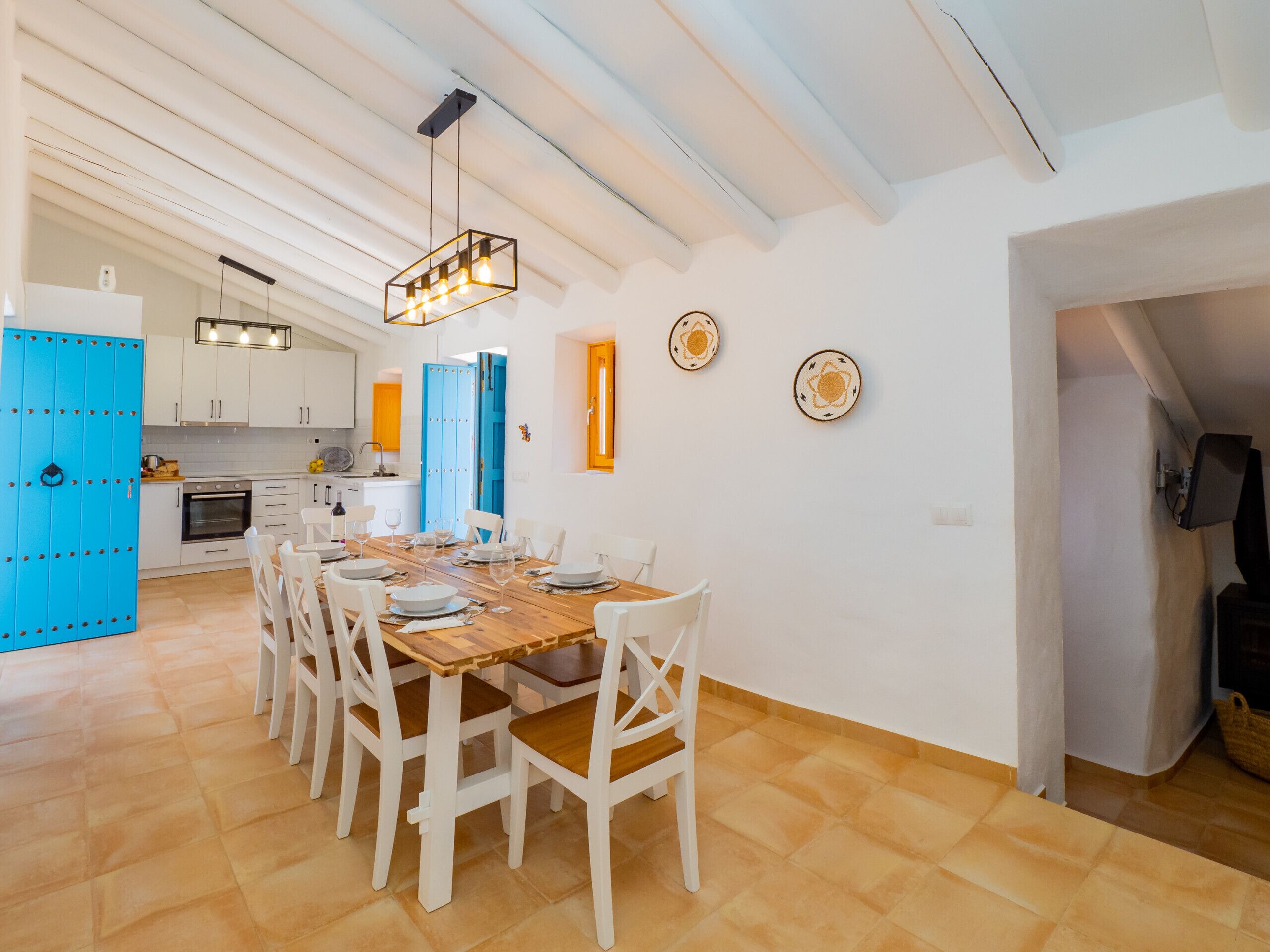 A spacious dining area with a wooden table and white chairs, a kitchen in the background, and a blue door.