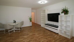 Ein modernes Wohnzimmer mit Essbereich, Holzböden, einem Flachbildfernseher und Einbauschränken.