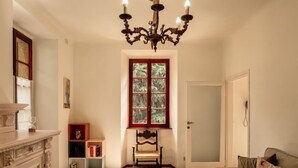 Ein Wohnzimmer mit Kamin, einer Kristallleuchter, einem Fenster mit geätztem Glas, einer Tür und einem Sofa mit einem floralen Kissen.