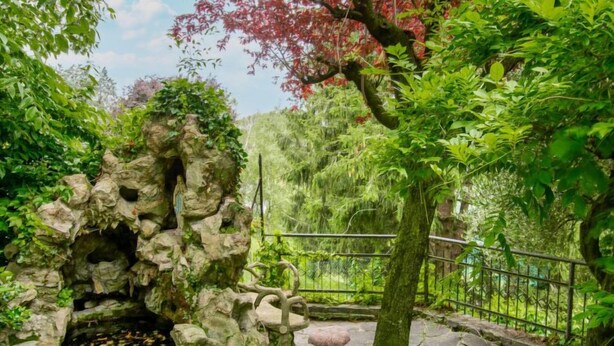 Ein Garten mit Felsformation, Stehbank und Metallzaun.