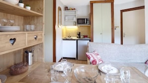 Una stanza compatta con un tavolo da pranzo per quattro persone, una zona cottura con forno a microonde e un divano con un cuscino decorativo.