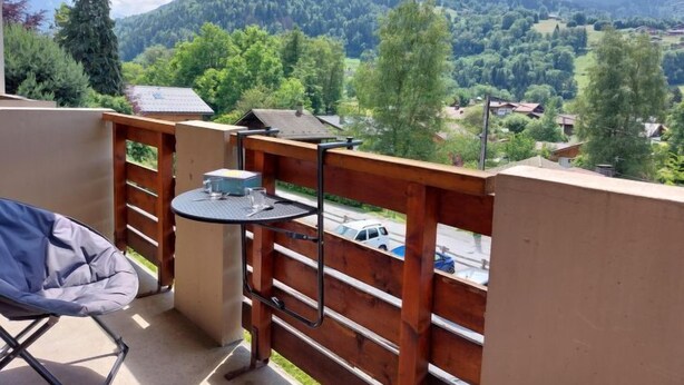 Un balcone con vista su un paesaggio montuoso, un tavolo con una sedia e un piccolo tavolino con un bicchiere e una scatola.