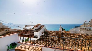 Una terraza en la azotea con vistas al mar, un banco de madera y una silla.