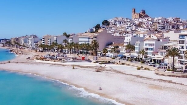 Un pueblo costero con playa, edificios blancos y palmeras.
