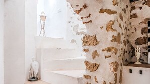 Una escalera con peldaños blancos que conduce a una plataforma, flanqueada por una pared blanca y una pared de piedra con parches.